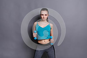 Fitness model woman with dumbbells at studio background