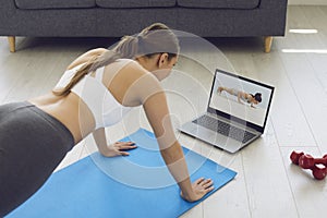 Fitness online. Young fit girl at home on the floor doing exercises, stretching warm-up and uses a video fitness lesson photo