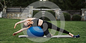 Fitness outdoors - woman stretching with fit ball at pilates workout in park. Sport girl hold fitball on green grass