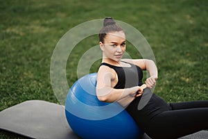 Fitness outdoors - woman stretching with fit ball at pilates workout in park. Sport girl hold fitball on green grass