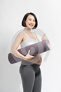 Fitness and pregnancy. Pregnant lady holding yoga mat smiling at camera standing on white studio background