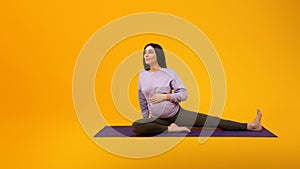 Fitness during pregnancy. Pregnant lady sitting on yoga mat and stretching legs, looking aside at free space, panorama