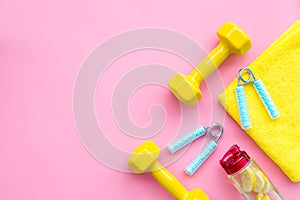 Fitness set with bars, towel, bottle of water and wrist builder on pink background top view mock up