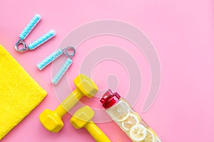 Fitness set with bars, towel, bottle of water and wrist builder on pink background top view mock up