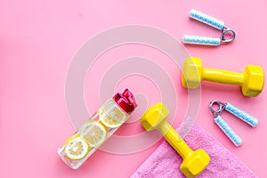 Fitness set with bars, towel, bottle of water and wrist builder on pink background top view mock up