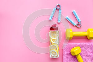 Fitness set with bars, towel, bottle of water and wrist builder on pink background top view mock up