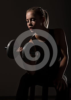 Fitness sexy girl with dumbbells on a dark background. Athlete doing exercises in the gym