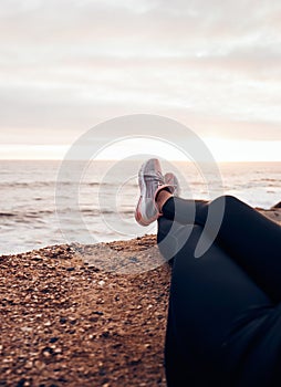 Fitness, shoes and beach in nature feeling relax with freedom outdoor sitting. Waves, ocean and water with a person and