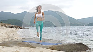 Fitness smiling woman doing sporty exercise on beach outside at sunset.