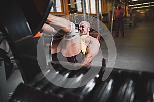 Fitness and Sport. Athletic man doing exercises on legs in gym among other people.