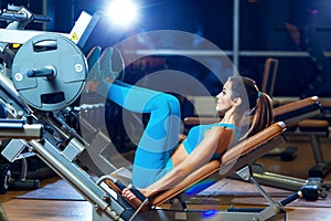 Fitness, sport, bodybuilding, exercising and people concept - young woman flexing muscles on leg press machine in gym