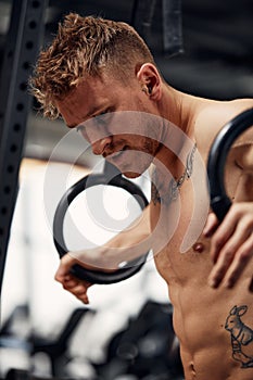 fitness, sport, bodybuilding and people concept - young man doing push-ups on gymnastic rings in gym.