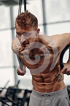 fitness, sport, bodybuilding and people concept - young man doing push-ups on gymnastic rings in gym.