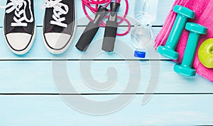 Fitness and sport concept. Apple, jump rope, dumbbells, bottle of water, sneakers and pink towel on blue wooden background. Free