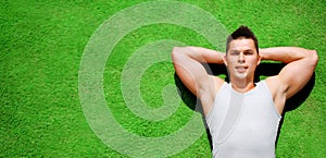 Fitness, sport concept - handsome sportsman relaxing lying on green grass, top view, blank copy space for advertising text