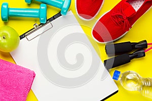 Fitness and sport concept. Red sneakers, apples, jump rope, dumbbells, bottle of water, pink towel and sheet of blank paper on