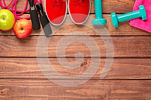 Fitness and sport concept. Red sneakers, apples, jump rope, dumbbells and pink towel on wooden background. Free space