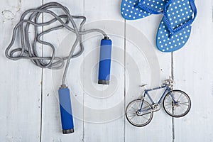 Fitness/sport and healthy lifestyle concept - Jumping/skipping rope with blue handles, flip flops in polka dots and model of