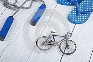 Fitness/sport and healthy lifestyle concept - Jumping/skipping rope with blue handles, flip flops in polka dots and model of