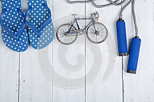 Fitness/sport and healthy lifestyle concept - Jumping/skipping rope with blue handles, flip flops in polka dots and model of