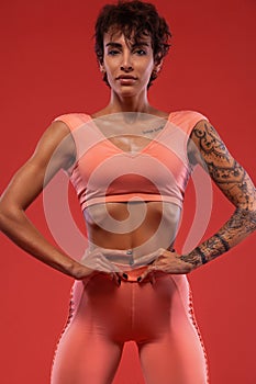 Fitness and sport motivation.. Strong and fit athletic, woman with tattoo posing on red background in sportswear.