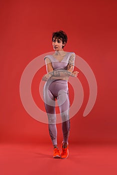 Fitness and sport motivation.. Strong and fit athletic, woman with tattoo posing on red background in sportswear.