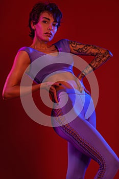 Fitness and sport motivation.. Strong and fit athletic, woman with tattoo posing on red background in sportswear.