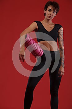 Fitness and sport motivation.. Strong and fit athletic, woman with tattoo posing on red background in sportswear.