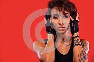 Fitness and sport motivation.. Strong and fit athletic, woman with tattoo posing on red background in sportswear with headphones.