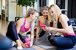 Fitness, sport, training, gym and lifestyle concept - group of happy women with bottles and smartphone in gym.