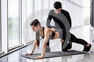 Fitness, sport, training, gym and lifestyle concept - smiling couple doing push-ups in the gym. Trainer work with woman to fo push