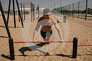 fitness, sport, training and lifestyle concept - young man exercising on horizontal bar on the beach