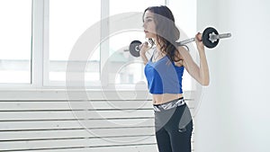 Fitness, sport, training and lifestyle concept - Young woman with barbell flexing muscles in white interior gym
