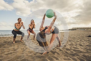 Fitness, sport, yoga and healthy lifestyle concept - group of people making pilates pose on beach. three young women doing