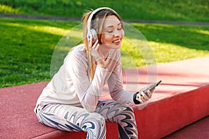 Fitness sports woman posing outdoors in park listening music with earphones using mobile phone