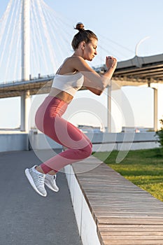 Fitness sporty female jump outdoors over urban street background. Slim woman doing cardio exercises