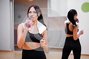 Fitness time. Beautiful young woman resting and drinking water in the gym