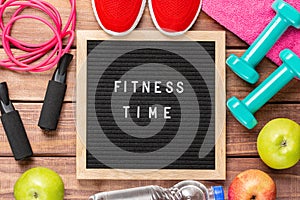 Fitness time and sport concept. Red sneakers, apples, jump rope, dumbbells, pink towel and black letterboard with words Fitness