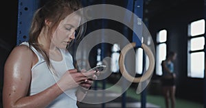 Fitness tracker app. Close-up tired sweaty Caucasian woman using smart phone to work with online coach at modern gym.