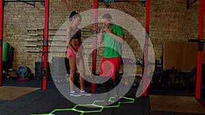 Fitness trainer showing side straddle hop exercise to woman using agility ladder