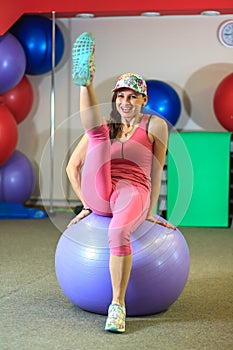 Fitness training. Young beautiful white girl in a pink sports suit does physical exercises with a violet fit ball.