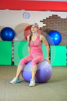 Fitness training. Young beautiful white girl in a pink sports suit does physical exercises with a violet fit ball.