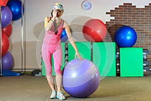 Fitness training. Young beautiful white girl in a pink sports suit does physical exercises with a violet fit ball.