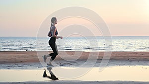 Fitness woman active running jogging cardio training outdoor sunset sand sea beach side view slowmo