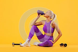 Fitness woman athlete and bodybuilder rest, holding dumbbell and shaker . Isolated on yellow background.