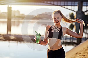 Fitness woman with bottle of water after running training on river and brige urban city background