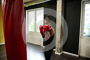 Fitness woman boxer in tight-fitting black sportswear and red boxing gloves training in a boxing gym, making a straight punch