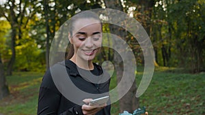 Fitness woman Caucasian sporty girl walking in city park with sport bottle drinking water using smartphone check mobile