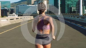 Fitness woman, city runner and training on a road of an urban bridge for a cardio workout from behind. Sport motivation