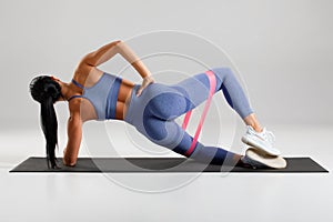 Fitness woman doing clamshell exercise for glutes with resistance band on gray background. Athletic girl working out